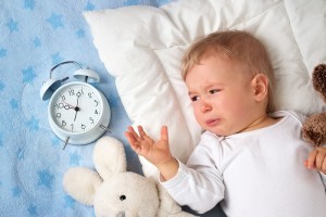 One year old baby lying in bed with alarm clock and crying